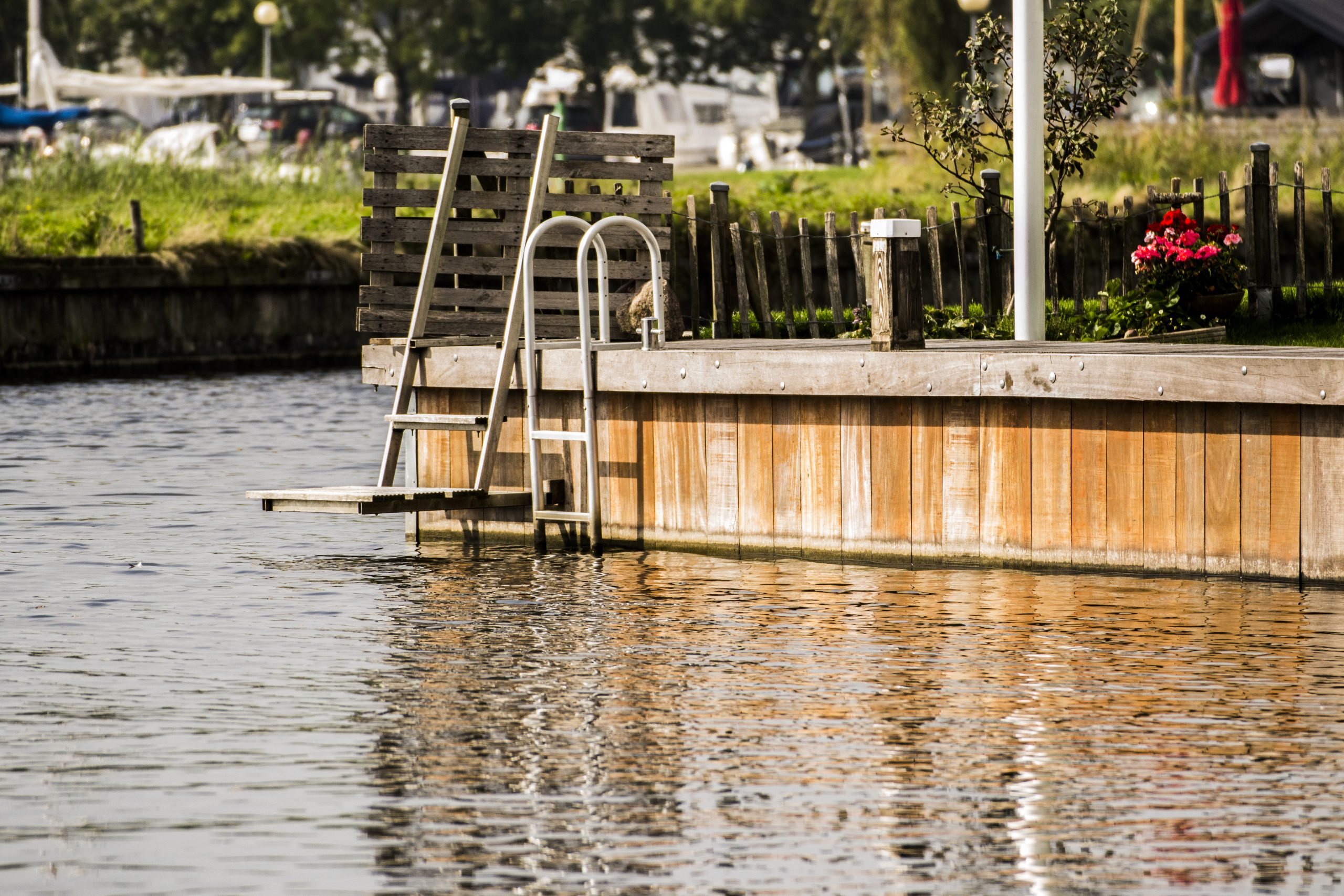 Houten steiger met roestvrijstalen trap aan het water, afgewerkt met bloembakken en beschoeiing.