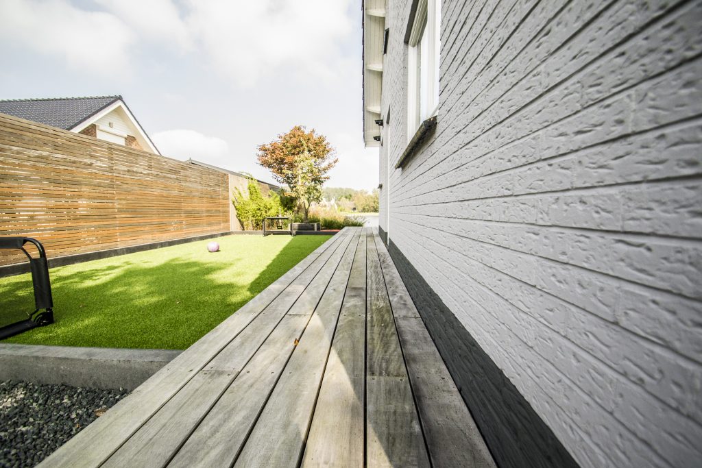 Modern houten terras met kunstgras tuin en grijze gevelbekleding bij woning