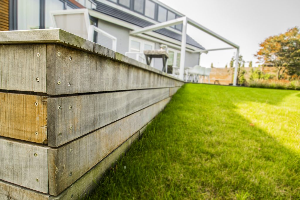 Houten keerwand van grijs vergrijsd hout naast gazon bij woonhuis, uitgevoerd door Bouma Waterwerken.