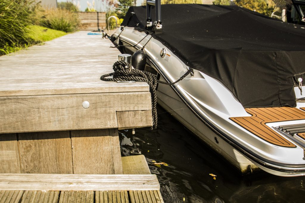 Motorboot afgemeerd aan houten steiger met touwbevestiging aan meerpaal langs waterkant.
