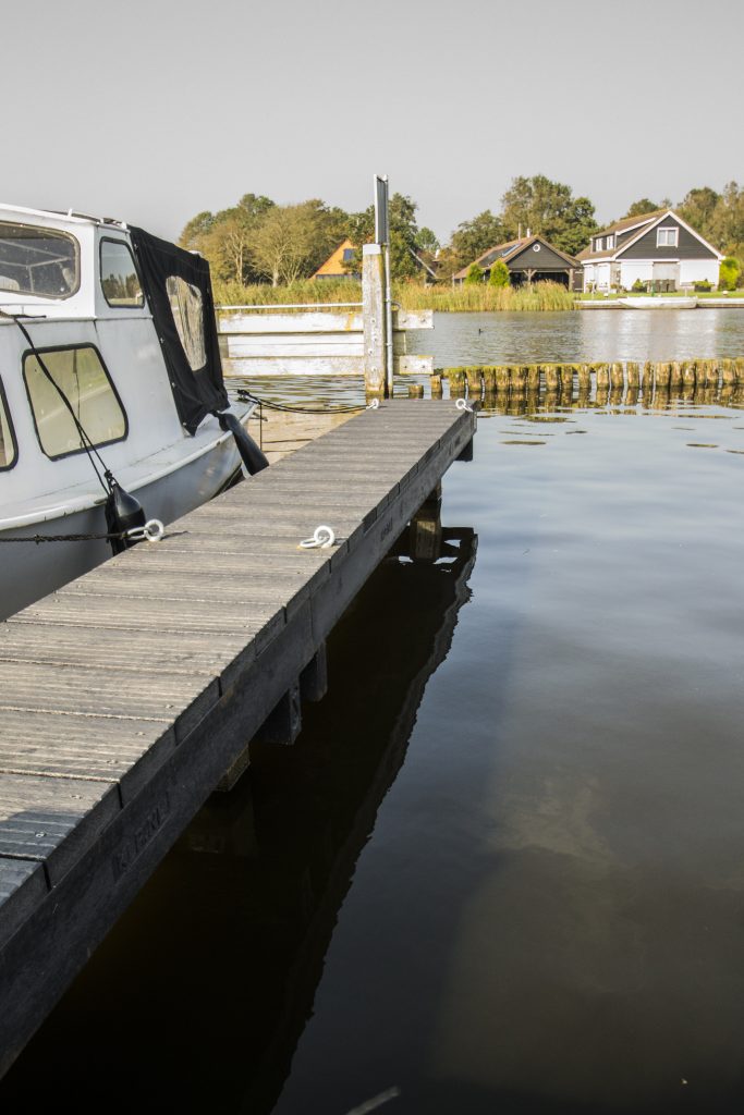 Houten steiger aan het water met een aangemeerde boot en een woning op de achtergrond.