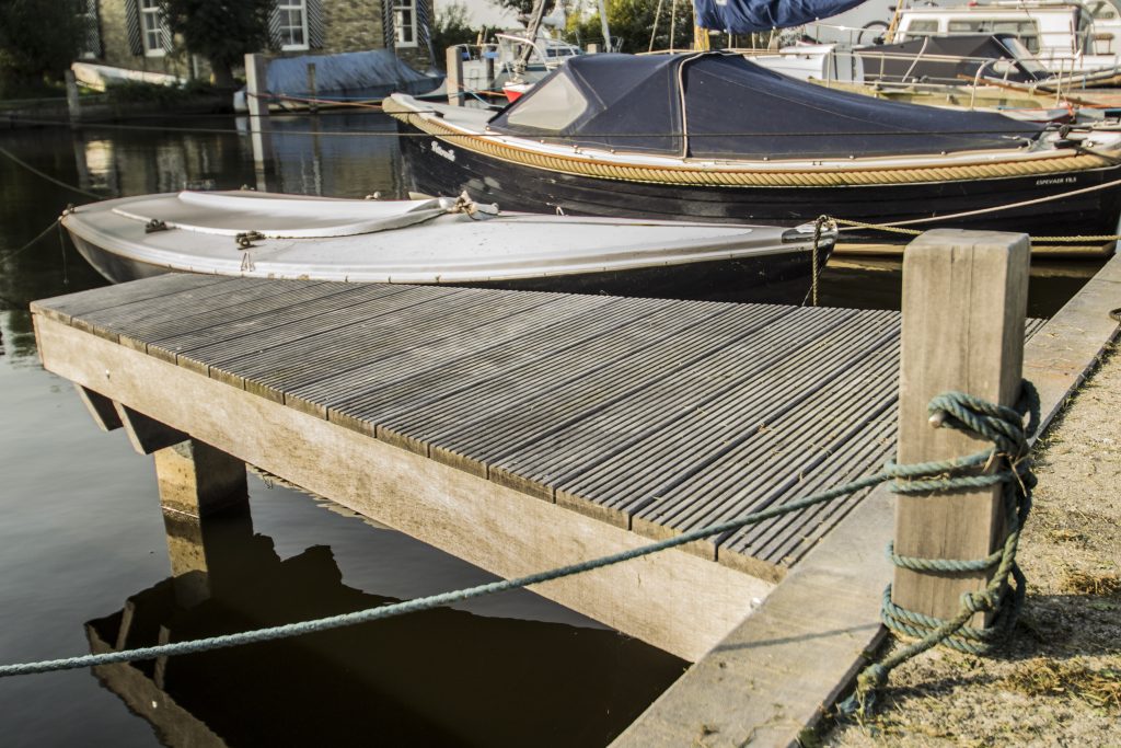 Nieuw aangelegde houten vlonderlandingssteiger aan het water met afgemeerde boten op de achtergrond.