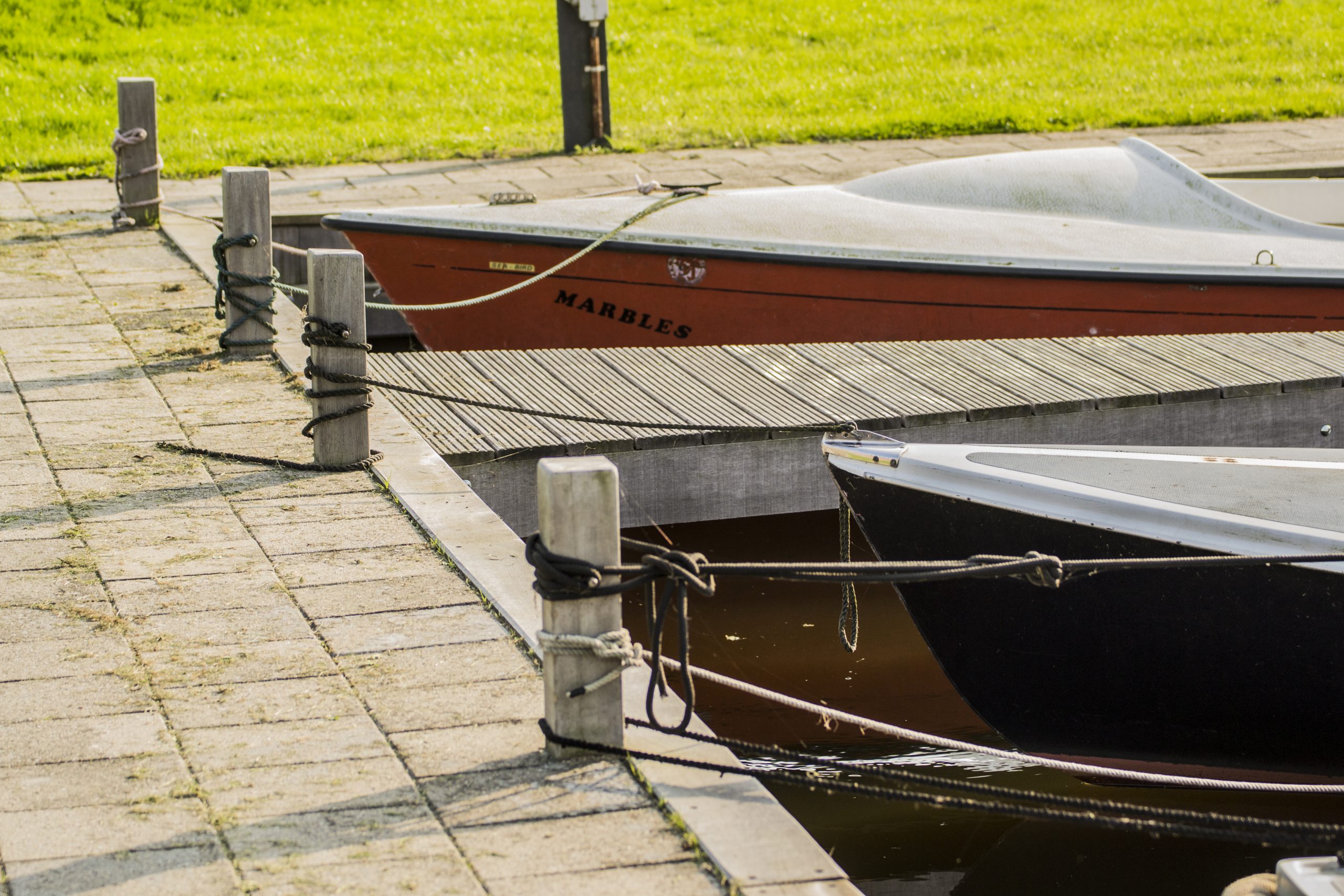 Houten en aluminium boten afgemeerd aan een betonnen steiger met meerpalen langs de kade.