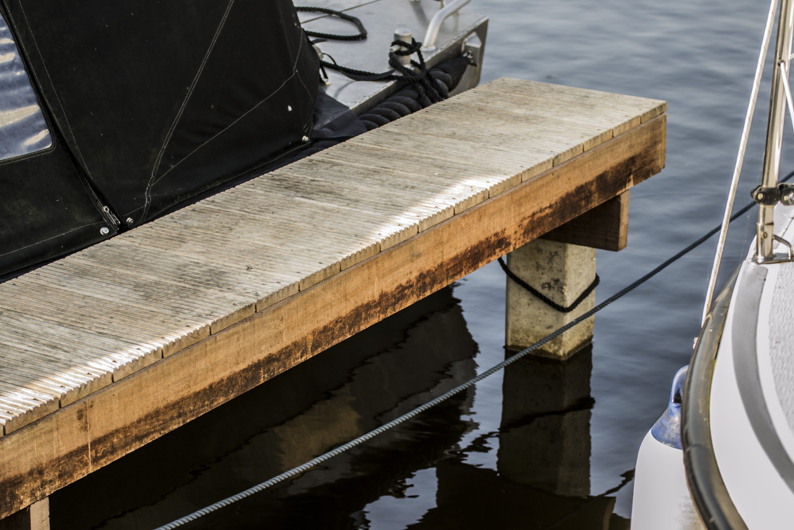 Verweerde houten steiger aan het water met betonnen palen, geparkeerde boten ernaast.