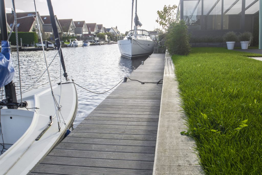 Houten steiger met aangemeerde zeilboten in jachthaven, met groen grasveld langs waterkant