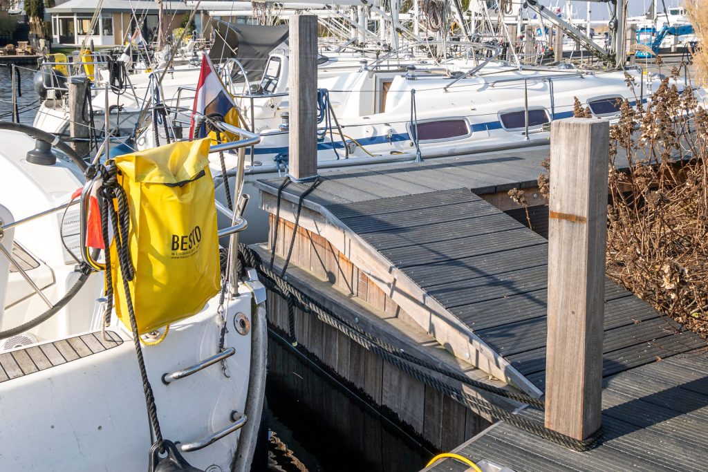 Houten steiger met gele reddingsboei en aangemeerde boot met zonnepanelen in jachthaven