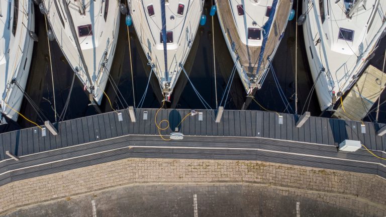 Luchtfoto van aangemeerde zeilboten aan steigers in jachthaven met betonnen kademuur