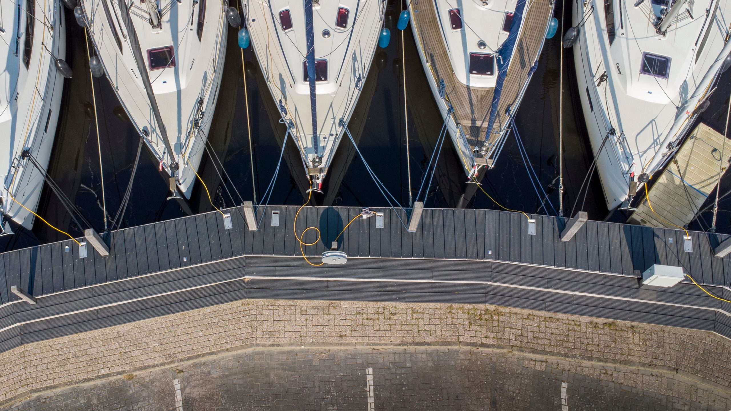 Luchtfoto van aangemeerde zeilboten aan steigers in jachthaven met betonnen kademuur