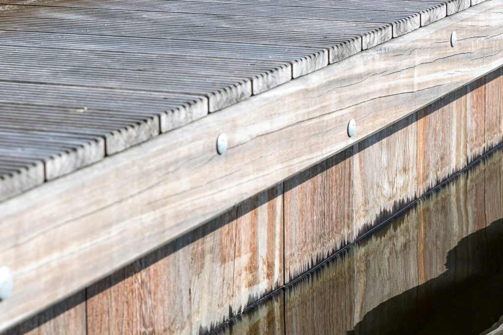 Close-up van verweerde houten steiger met planken en beschoeiing langs het water, uitgevoerd door Bouma Waterwerken.