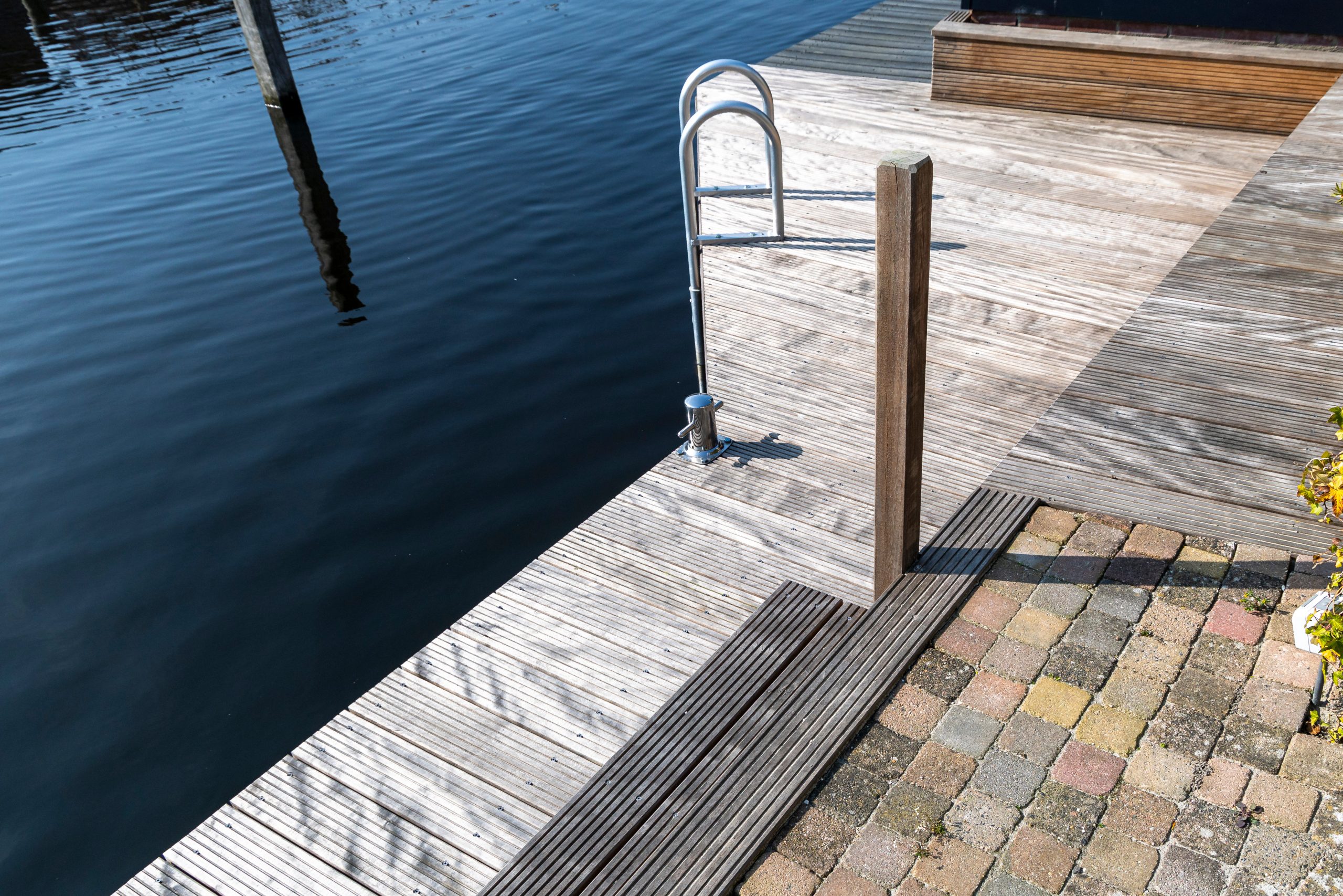 Houten steiger met roestvrijstalen instaplader aan het water, aangelegd door Bouma Waterwerken.