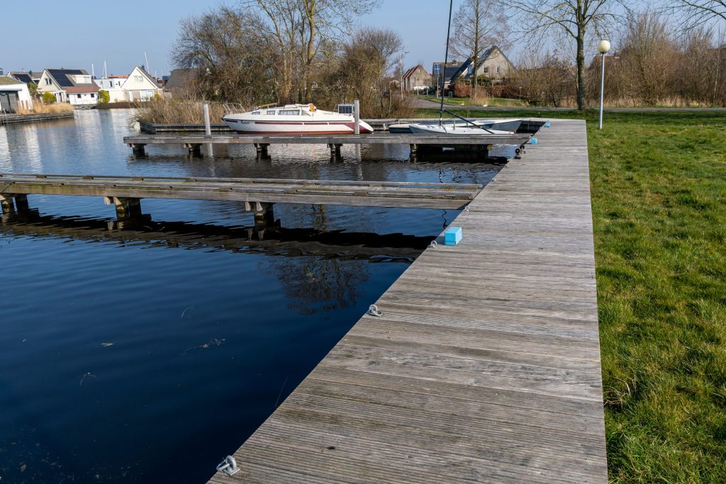 Houten steiger langs het water met aangemeerde boten, aangelegd door Bouma Waterwerken.