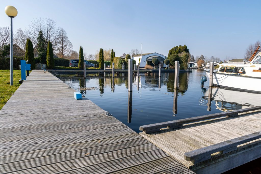 Houten aanlegsteiger langs rustige jachthaven met boten en helder water op zonnige dag.