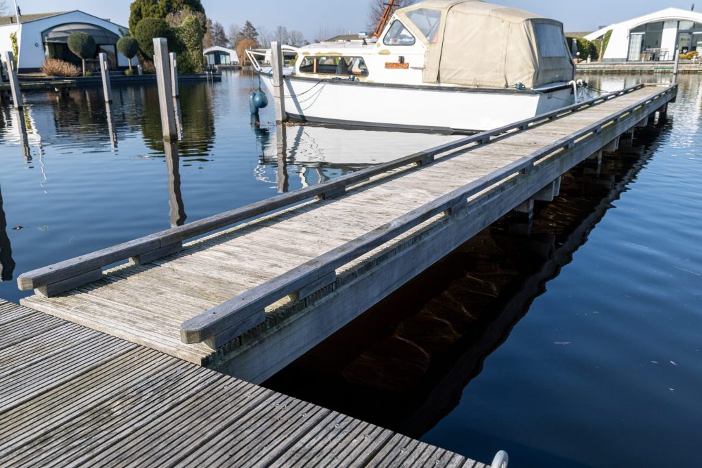 Houten steiger langs het water met afgemeerde boot, aangelegd door Bouma Waterwerken.