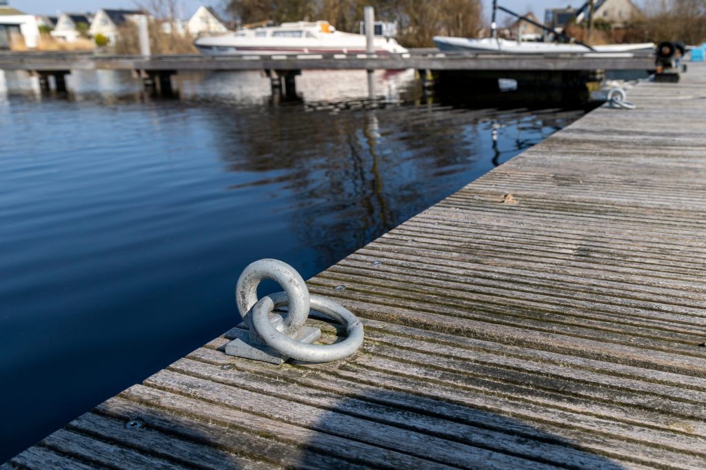 Metalen afmeerring op houten steiger langs open water, gebruikt voor het vastleggen van boten.
