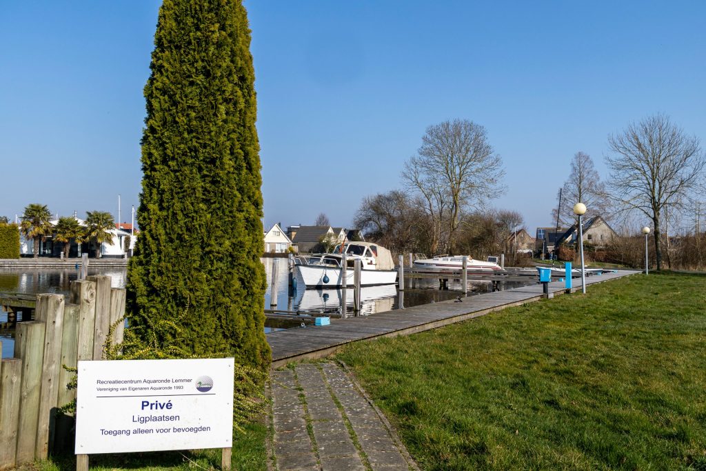 Privé jachthaven met aangemeerde boten langs houten steiger, omgeven door groen landschap.