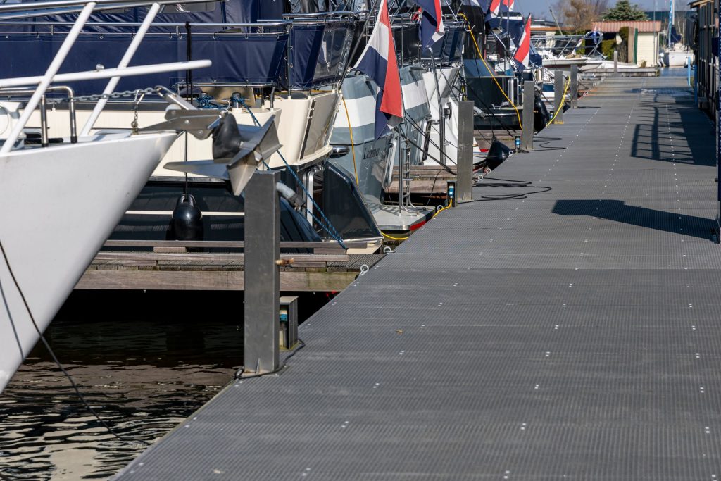 Drijvende steiger met antislip dekplaten langs afgemeerde zeilboten in jachthaven