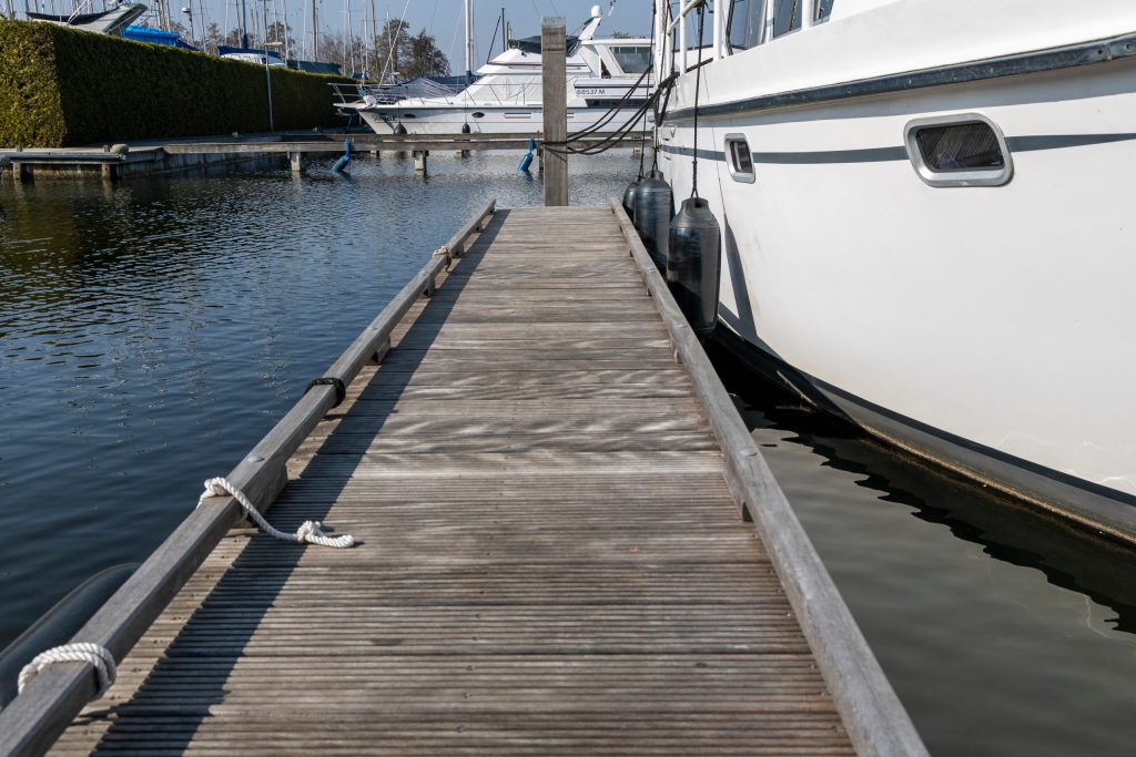 Houten steiger langs afgemeerde boot in jachthaven, aangelegd door Bouma Waterwerken.