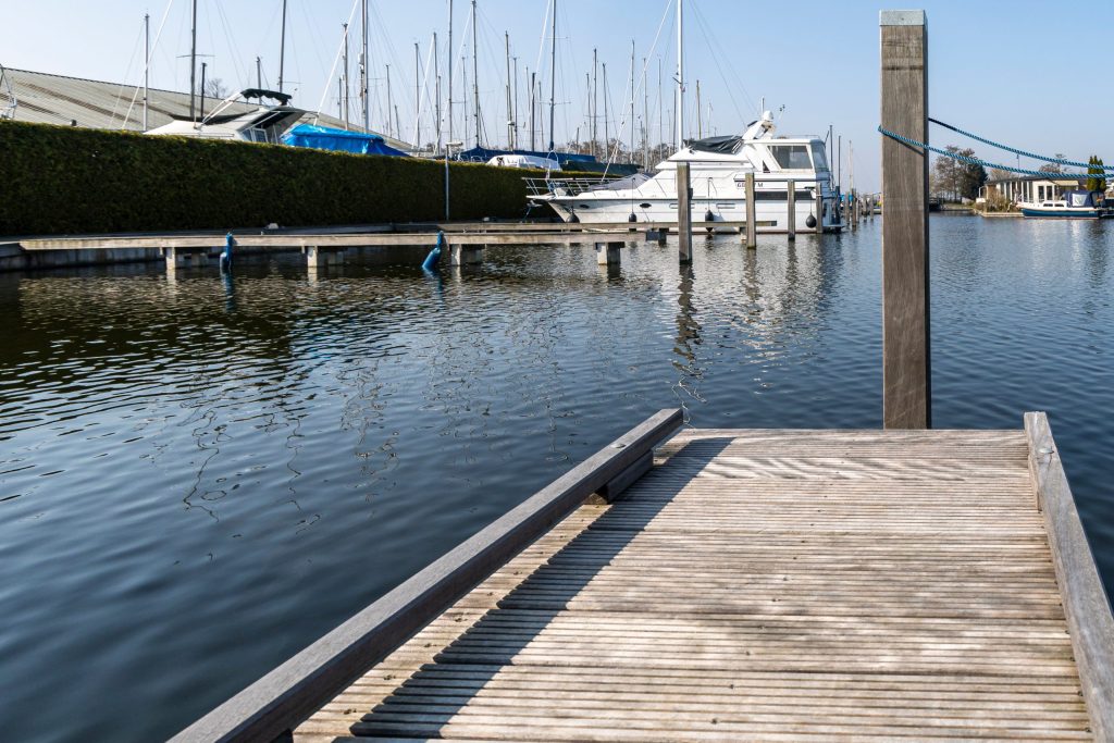 Houten steiger in jachthaven met afgemeerde boten en helder water op zonnige dag.