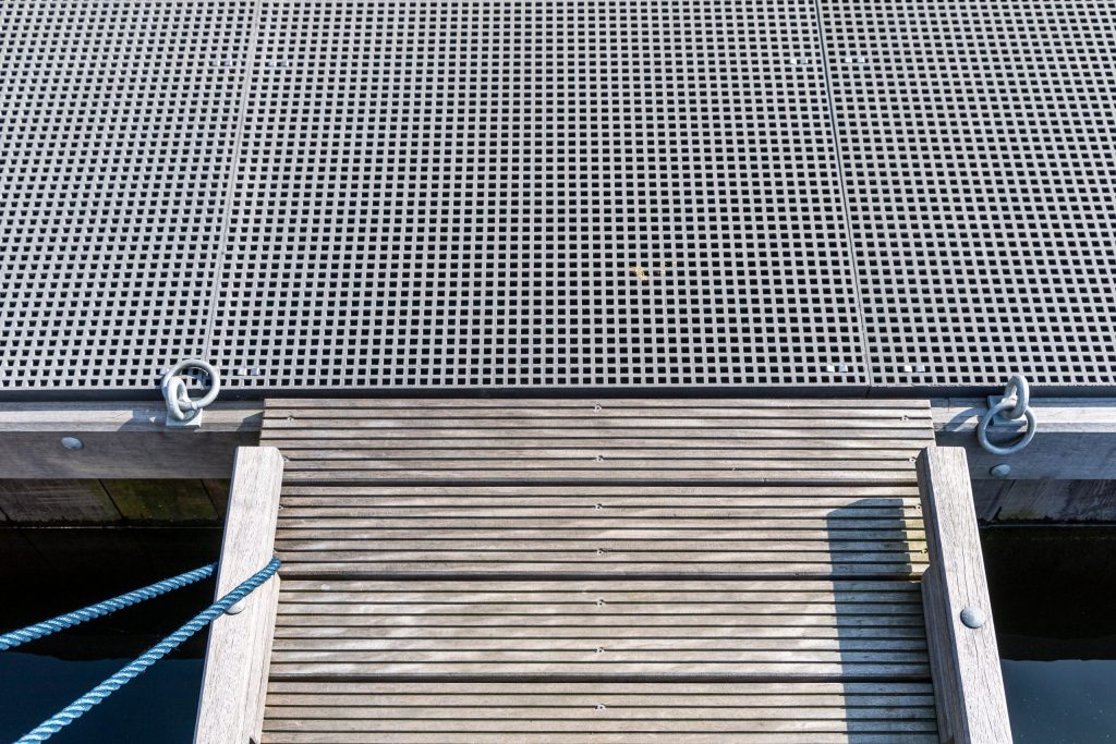 Aluminium geperforeerd drijvend steiger platform met houten loopplank en blauwe afmeerlijnen bij waterwerk.