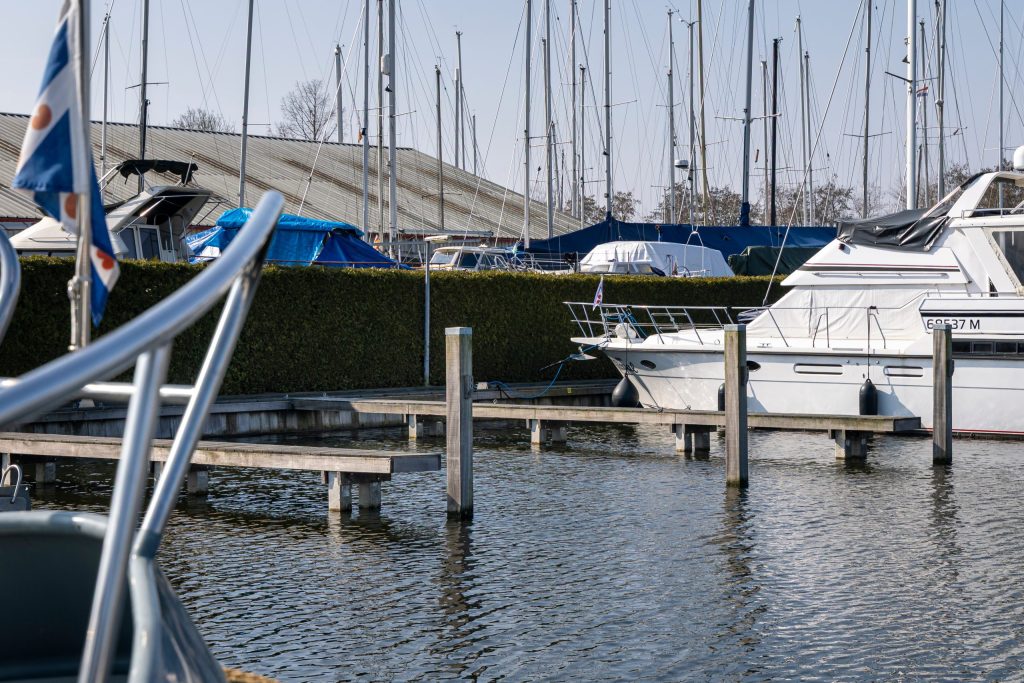 Houten steigers in een jachthaven met afgemeerde zeil- en motorboten op kalm water.