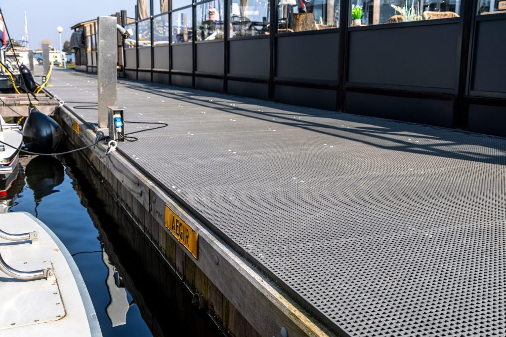 Drijvend werkplatform met antislip roosterplaten langs kade, afgemeerd naast boot in haven.