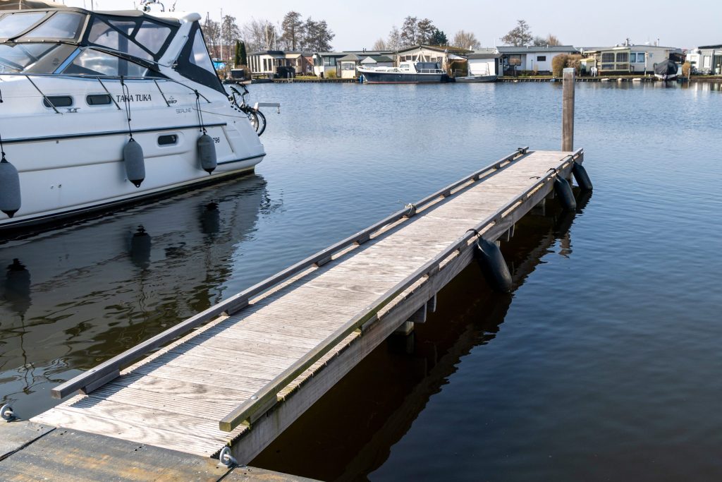 Houten aanlegsteiger in rustige jachthaven met afgemeerde motorboot en waterwoningen op achtergrond.