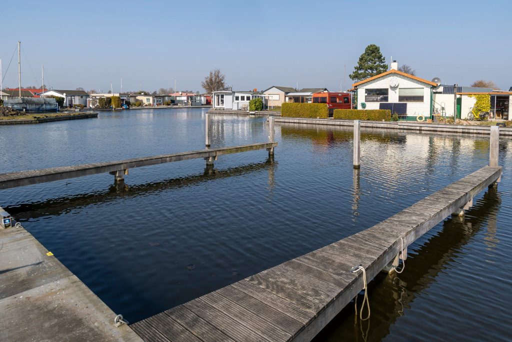 Houten vlondersteigers in rustige jachthaven met woningen op de achtergrond, uitgevoerd door Bouma Waterwerken.