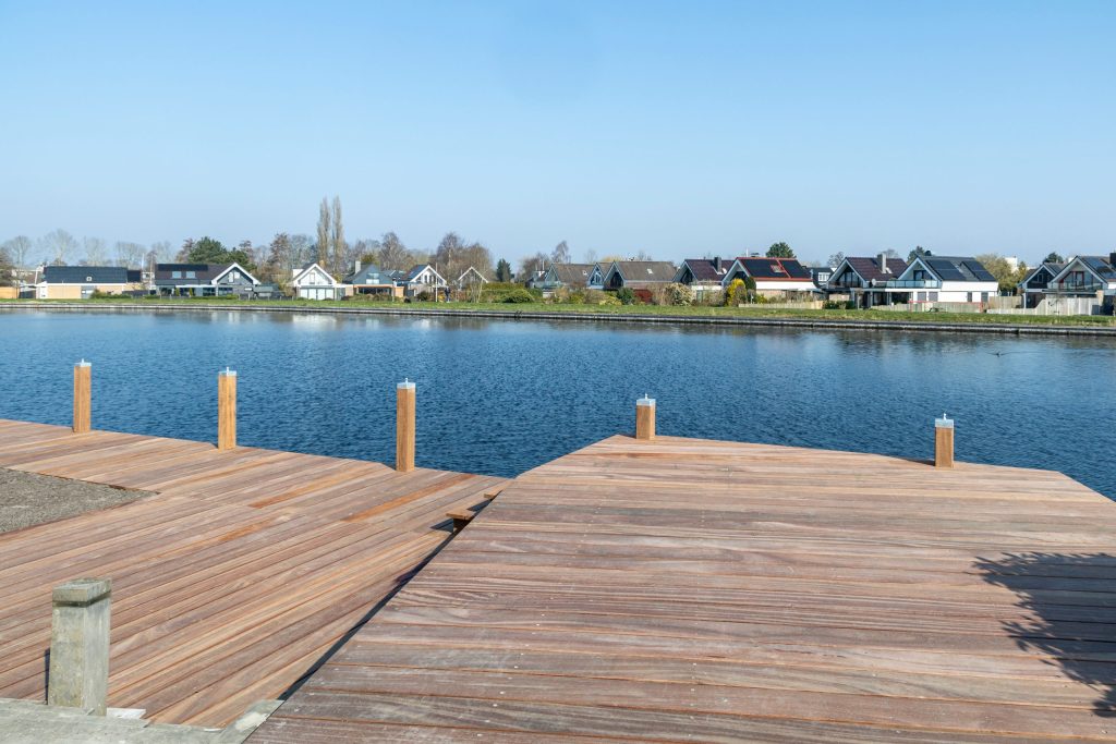 Nieuw aangelegde houten vlonder steiger aan rustig water met woningen op achtergrond.