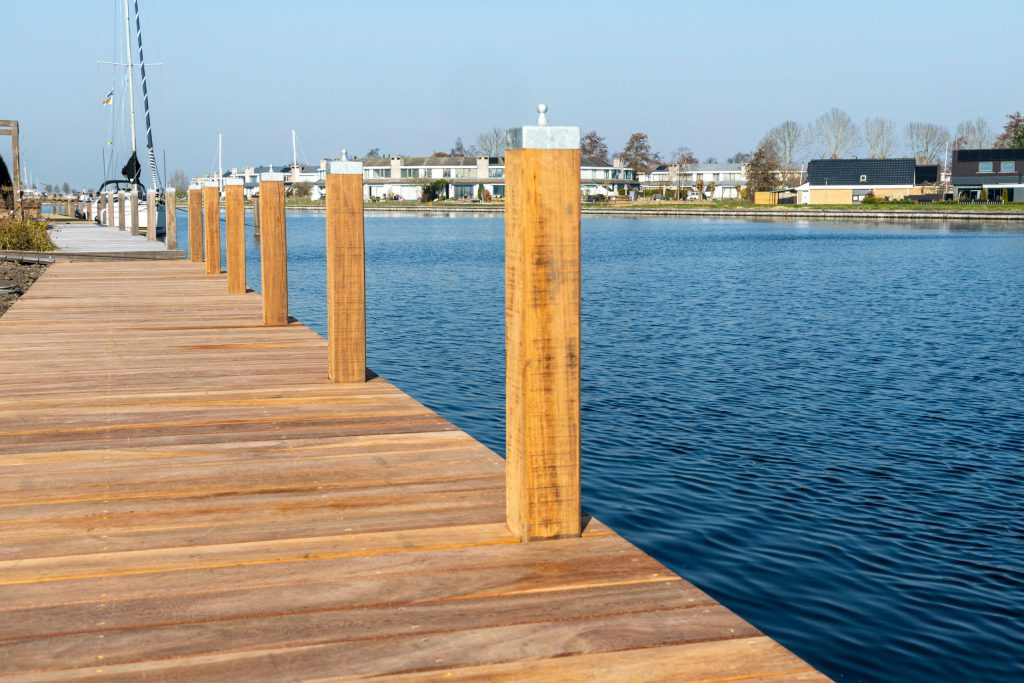 Nieuw aangelegde houten steiger met palen aan het water, met woningen op de achtergrond.