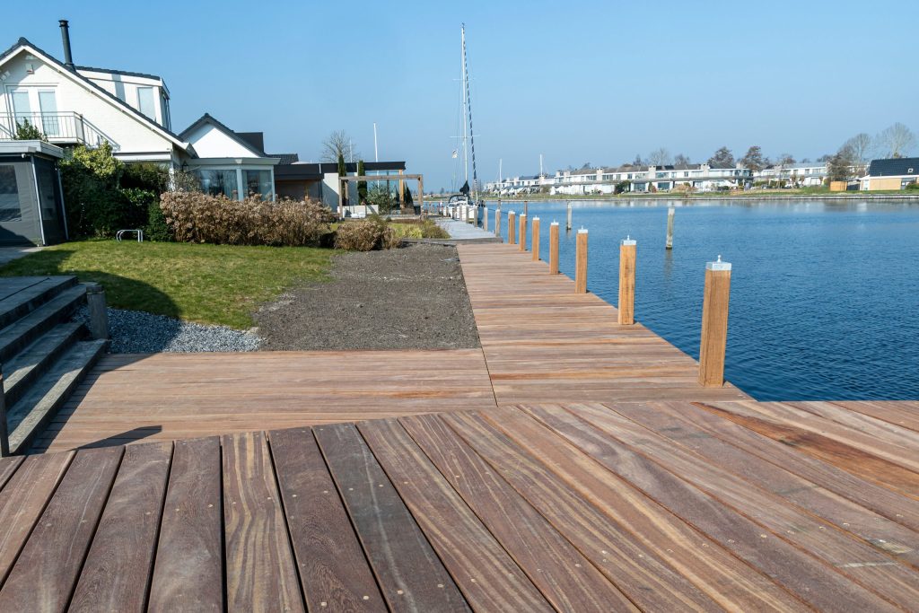 Nieuw aangelegde houten steiger langs het water met aanlegpalen bij een woonwijk door Bouma Waterwerken.