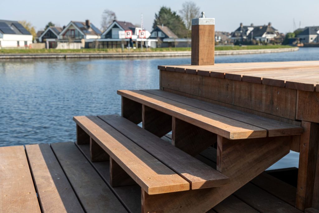 Houten steiger met trappen aan het water, omgeving met woningen op de achtergrond.