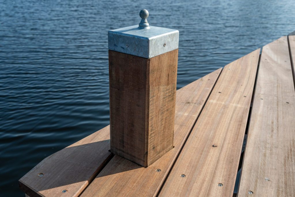 Houten meerpaal met roestvrijstalen meerpunt op steiger aan het water voor afmeren van boten