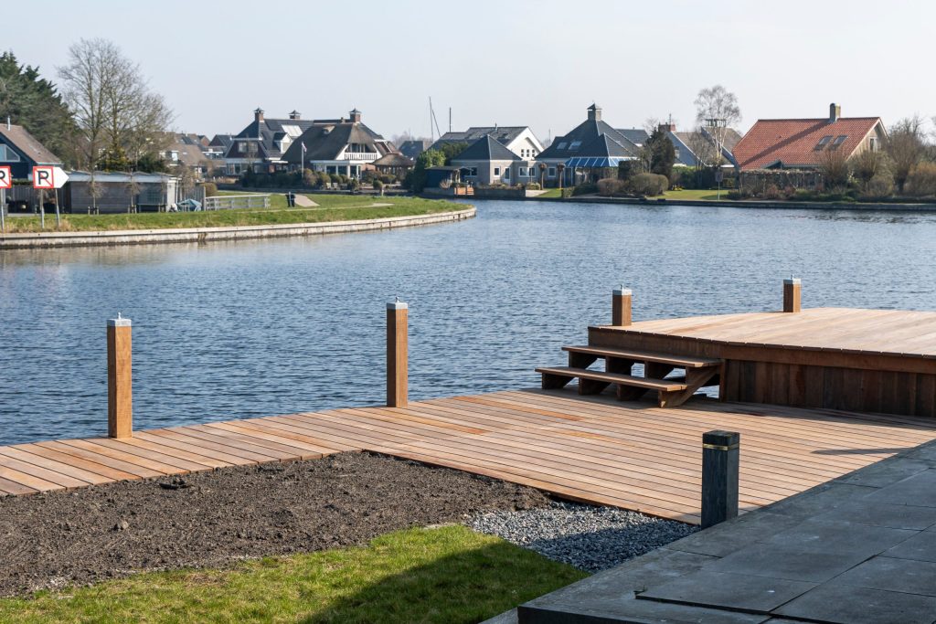 Nieuw aangelegde houten vlondersteiger aan rustige waterplas met woonhuizen op achtergrond.