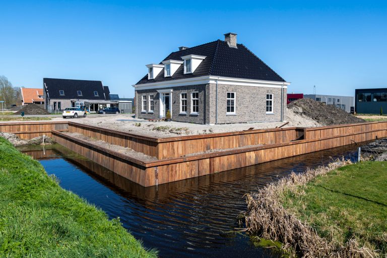 Nieuwbouw woning omringd door houten beschoeiing en waterpartij, professioneel aangelegd door Bouma Waterwerken.