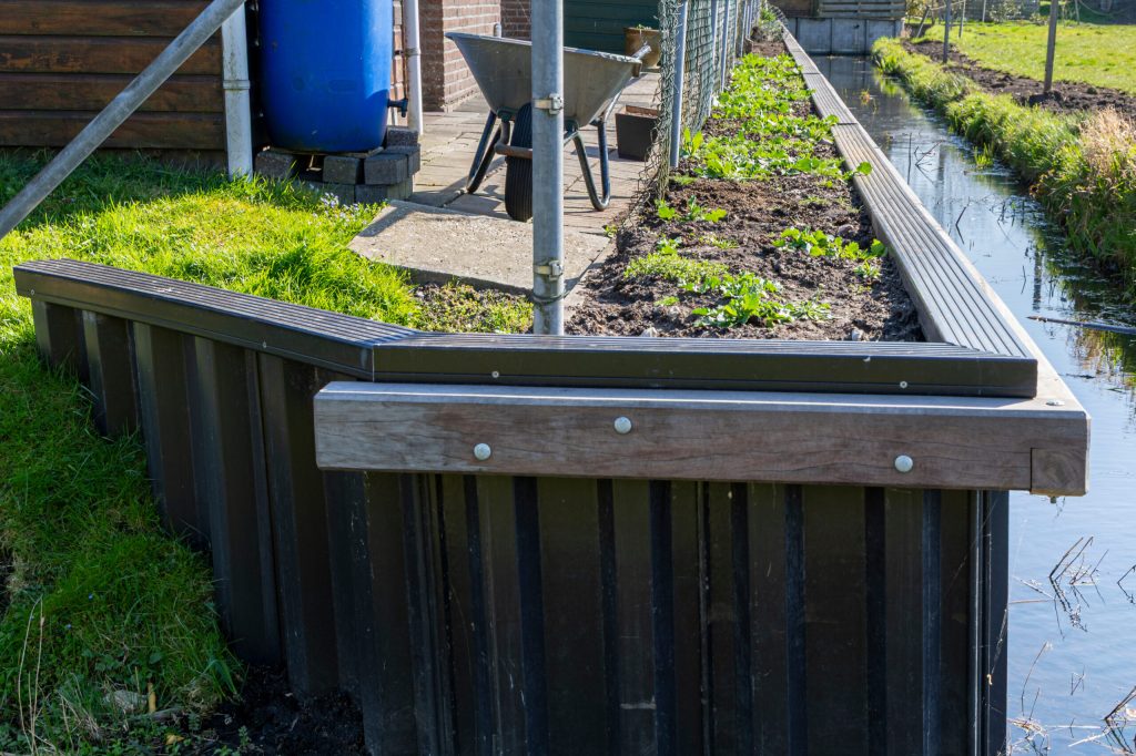 Drijvend verhoogd moestuinbed van donker hout met groene planten, langs een waterkanaal.