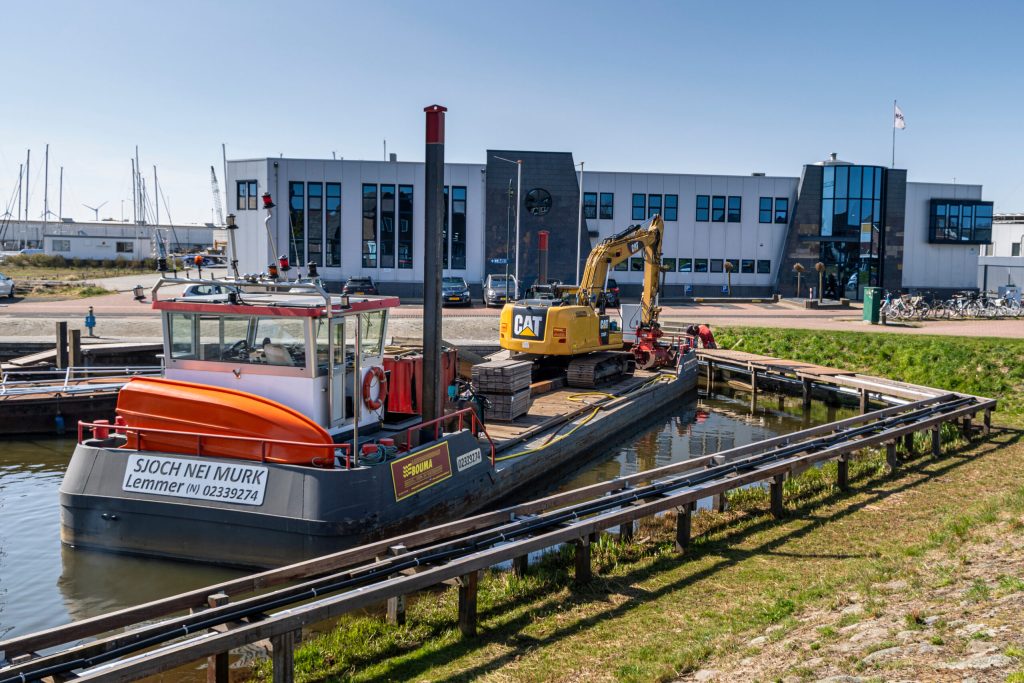 Baggerschip met gele CAT-kraan in haven, ingezet voor waterbodem werkzaamheden door Bouma Waterwerken.