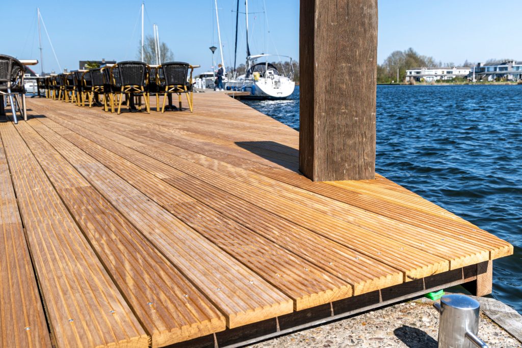 Nieuw aangelegde hardhouten steiger aan het water met afgemeerde zeilboten op de achtergrond.