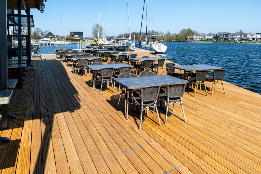 Hardhouten terras vlonder aan het water met tafels en stoelen bij jachthaven, gerealiseerd door Bouma Waterwerken.